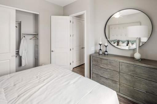 A white bedroom with a round mirror and a dresser.
