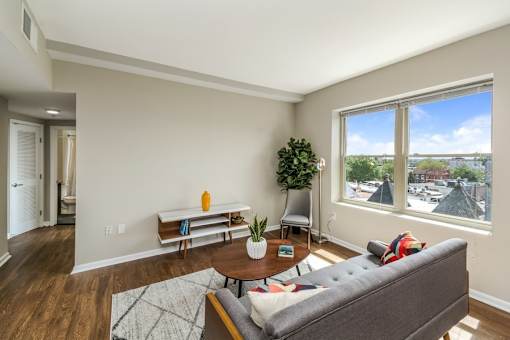 A living room with a grey couch, a wooden table, and a window with a view of the city.