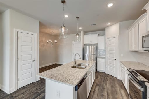 Gallatin, TN, Apartments - The Gardens at Preston Park - Modern Kitchen with Vinyl Plank Flooring, Quartz Countertops, White Cabinetry, Stainless Steel Appliances, Tile Backsplash, Large Island, and Pendant Lights.