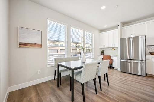 A kitchen with a dining table and chairs in the foreground and a refrigerator in the background.