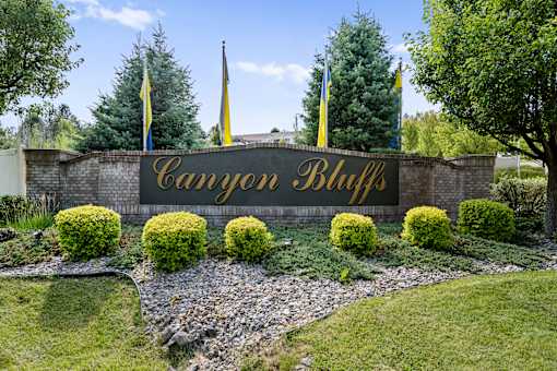 A sign that says Canyon Bluff in gold letters is surrounded by bushes and flags.