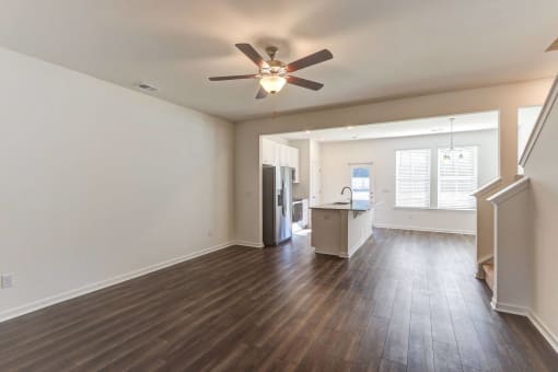 an empty living room with a ceiling fan and a kitchen