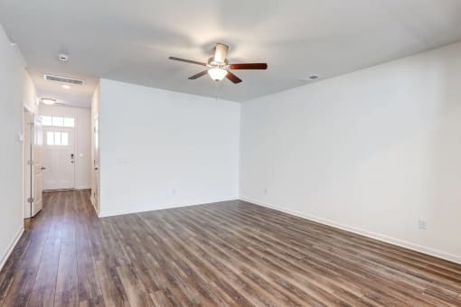 Four-BR Townhomes in North Charleston, SC - Highland Townhomes - Empty Living Room With White Walls, Wood-Style Flooring, and A Ceiling Fan