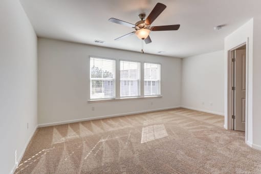 an empty living room with a ceiling fan and three windows