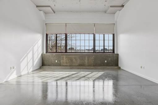 A large empty room with a concrete floor and a window with bars.