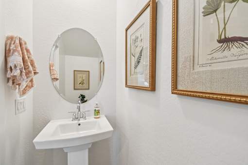 A bathroom with a sink, mirror, and two framed pictures on the wall.