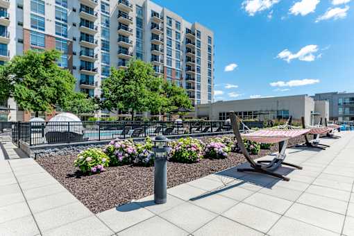 A sunny day at a modern apartment complex with a pool, trees, and benches.