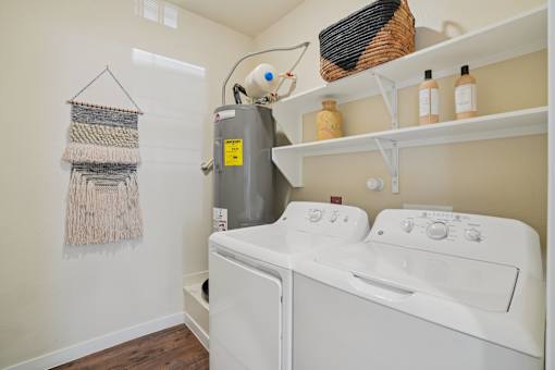 A laundry room with a washer and dryer, a basket on the shelf, and a wall hanging.