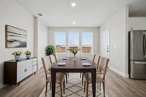 A dining room with a table set for six and a view of the outdoors through the windows.