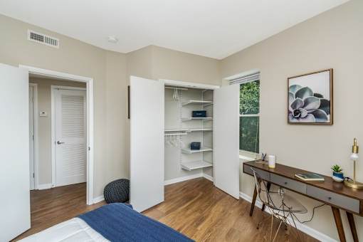 A room with a desk, chair, and a bed with a blue blanket.