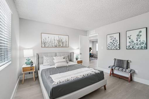 One-Bedroom Apartments in North Mountain Village, Phoenix, AZ - Ardella on 28th - Spacious Bedroom With Upholstered Bed, Side Tables, Lamps, Soft Gray Bedding, Bed Bench, and Large Window With Blinds.