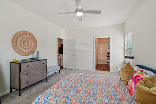 A bedroom with a colorful bedspread and a ceiling fan.
