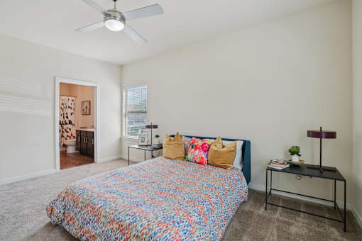 A bedroom with a bed, a fan, and a small table.