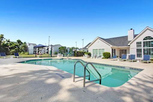 A swimming pool in front of a house with a blue sky.