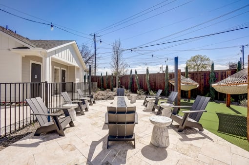  Two-Bedroom Homes For Rent In Denton, TX - Carmel Villas - Firepit With Strung Outdoor Lights Surrounded By Chairs Next To Hammocks Above Turf