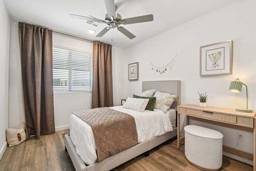 A bedroom with a bed, desk, and window with curtains.