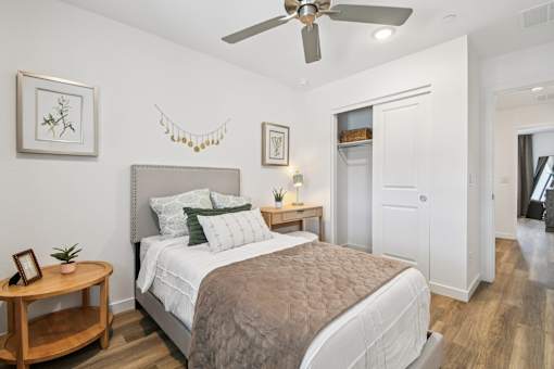 A bedroom with a bed, a ceiling fan, and a wooden side table.