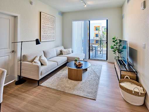Bright living room at Gateway Luxury Apartments in Pompano Beach, featuring large sliding glass doors that open to a private balcony and fill the space with natural light.