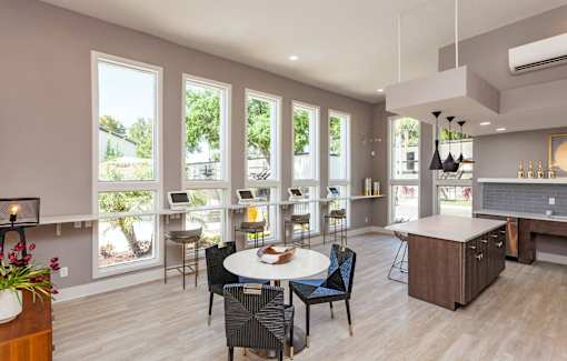 A modern kitchen with a dining table and chairs in the foreground and a balcony with a view of trees and a house in the background.