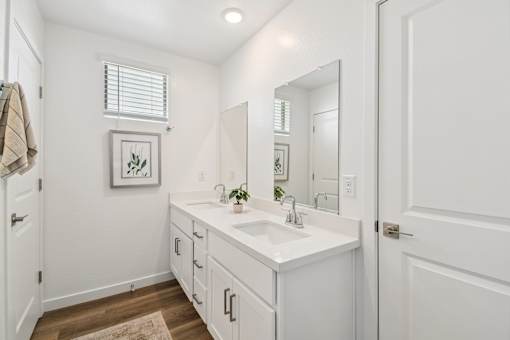 A white bathroom with a sink, mirror, and a rug on the floor.