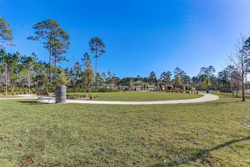 a park with a bench and a trash can in the middle of a grassy area