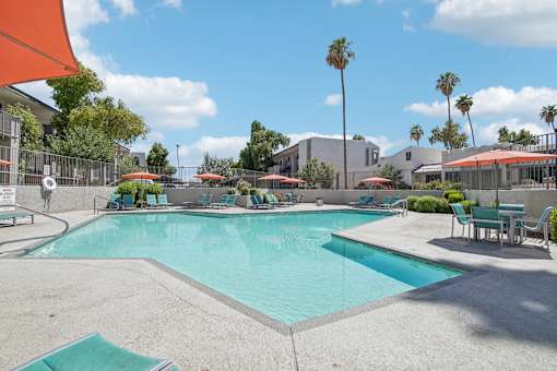 Phoenix Apartments - Ardella on 28th - Gated Outdoor Pool Area with Lounge Seating, Umbrellas, Tables with Chairs, and Surrounding Trees.