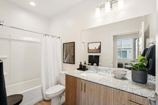 A bathroom with a white toilet, a sink, a mirror, and a window.