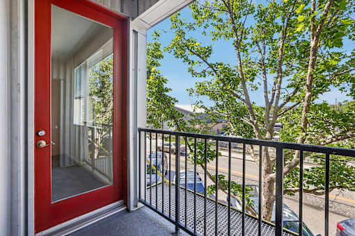 A red door is open to a balcony with a black railing.
