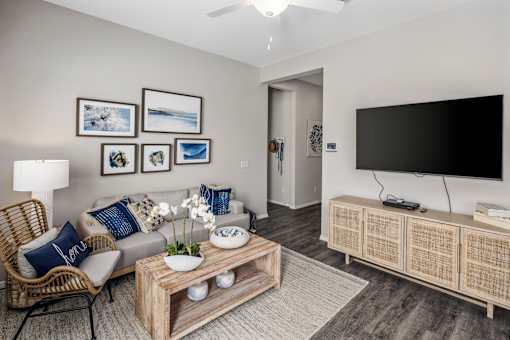 Apartments for Rent in Phoenix AZ - The Crofton at Sheely Farms - Spacious Living Room with a Grey Sofa, Wooden Coffee Table, Armchair, TV Monitor, Mounted TV, and a Ceiling Fan