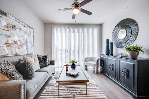 A living room with a grey couch, a coffee table, a ceiling fan, and a large abstract painting on the wall.