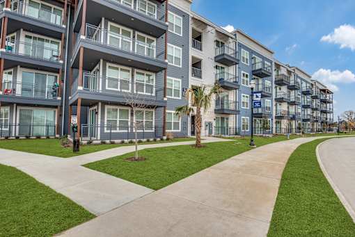 A modern apartment complex with a well-maintained lawn and walkway.