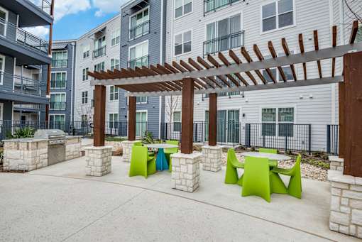 A patio with a pergola and green chairs.