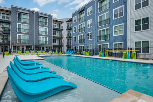 A swimming pool with blue loungers in front of apartment buildings.