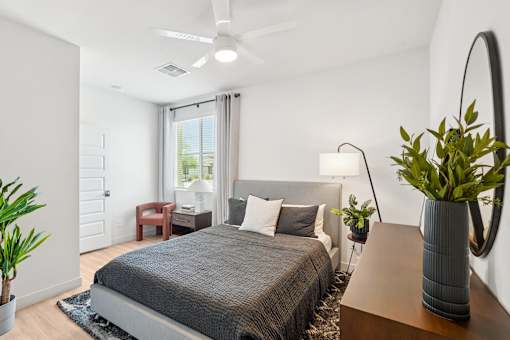 A bedroom with a bed, a chair, a lamp, and a potted plant.