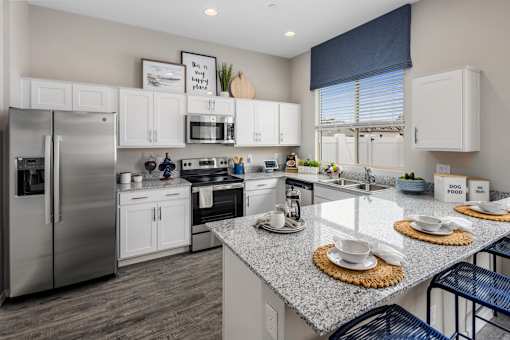 Phoenix AZ Apartments for Rent - The Crofton at Sheely Farms - Modern Kitchen with Stainless Steel Appliances, Granite Countertops, White Cabinetry, Dual Sink, Chairs, and a Nearby Window