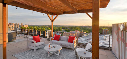 A wooden pergola over a patio with white furniture and a view of the city.