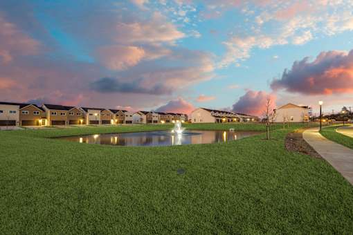 A row of houses with a grassy area in front and a pond in the middle.