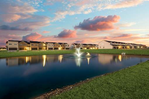 A serene lakeside view of a residential area with houses and a fountain.