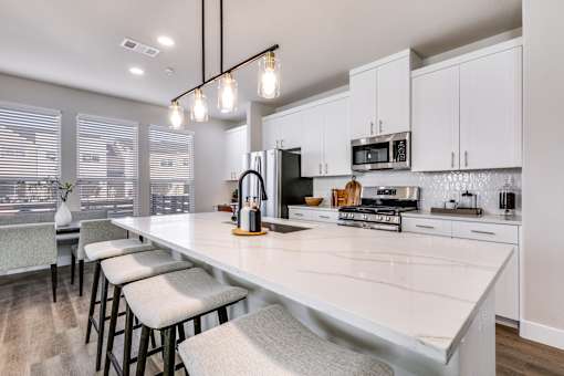 A kitchen with white cabinets and a long island with bar stools.
