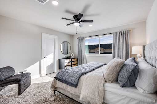 A bedroom with a bed, chair, and a ceiling fan.