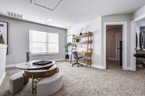 A living room with a grey carpet and a round table with a plant on it.