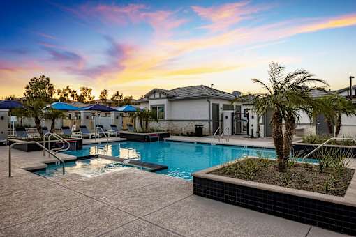 Phoenix AZ Apartments - The Crofton at Sheely Farms - Large Pool with a Hot Tub, Fountains, Plant Beds, Poolside Lounge Chairs, and Umbrellas, Shot at Sunset