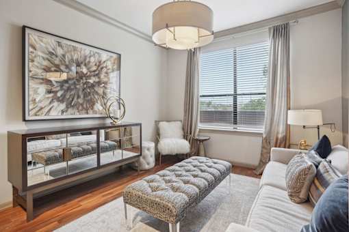 A living room with a grey sofa, a grey rug, a grey coffee table, a grey side table, a grey armchair, a grey chair, a grey lamp, a grey wall, a grey floor, a grey ceiling,