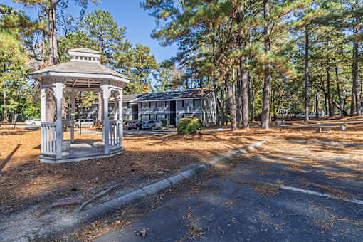 A gazebo sits in the middle of a paved area with trees in the background.