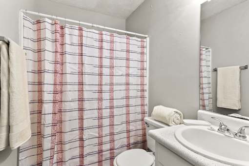 A white bathroom with a red and white checkered shower curtain.