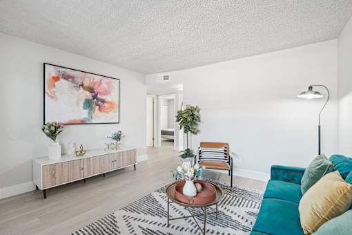 Two-Bedroom Apartments in North Mountain Village, Phoenix, AZ - Ardella on 28th - Bright Living Room With Teal Sofa, Accent Chair, Coffee Table Decor, Media Console, and Modern Wall Art.