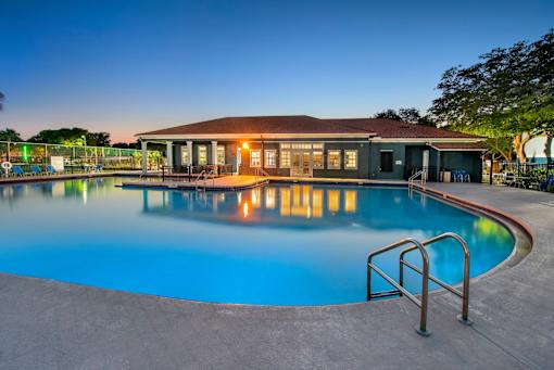 A swimming pool in front of a building with lights on.