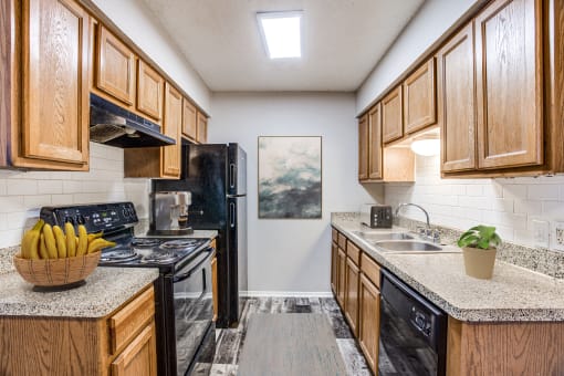 Apartments for Rent in Fort Worth- Monarch Pass- Kitchen with Black Appliances, Wooden Cabinets, and Tile Backsplash