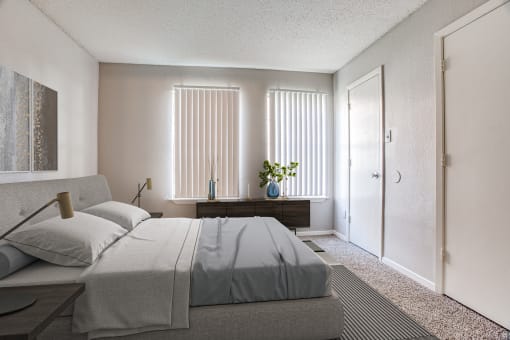 Fort Worth TX Apartments - Monarch Pass - Bedroom with Wall-to-wall Plush Carpeting, Beige Walls, Large Bed, and Windows with Vertical Blinds