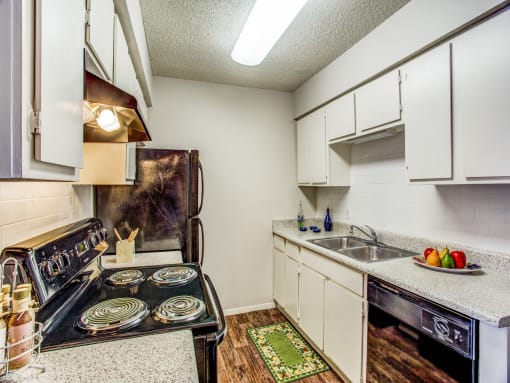 Apartments in Fort Worth TX - Monarch Pass - Kitchen with Wood-Style Floor, Black Appliances, Wooden Cabinets, and Double-Sink with Speckled Countertop